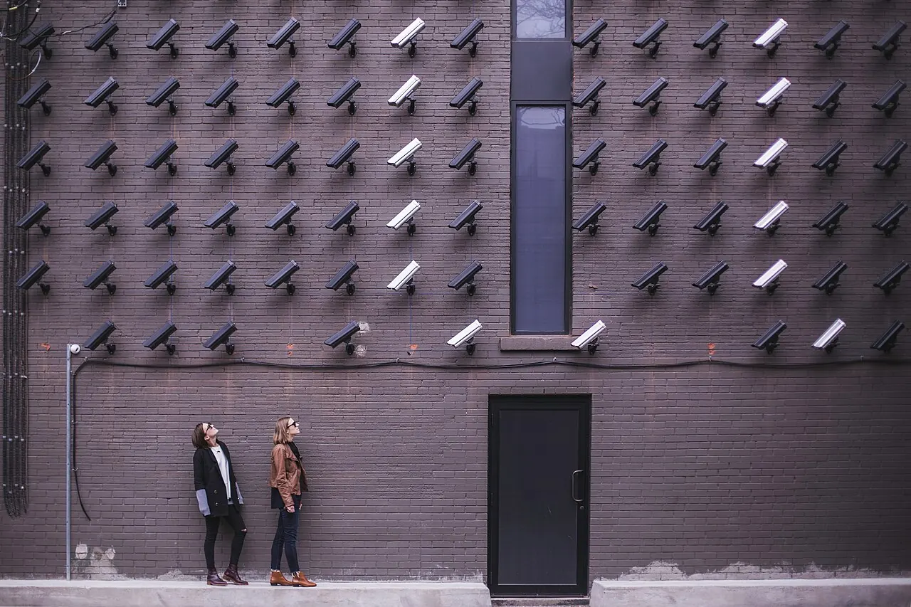 Two people look up at a wall covered in dozens of surveillance cameras